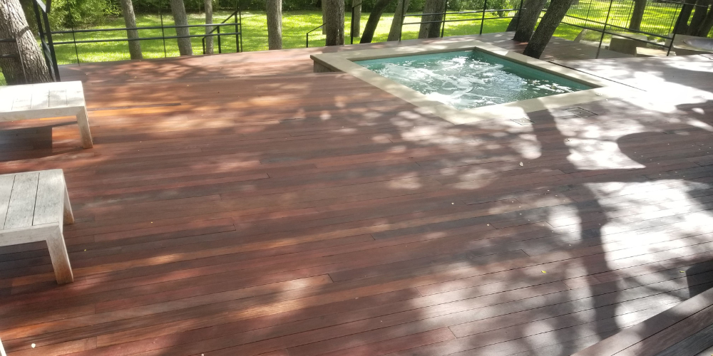 Freshly pressure‑washed hardwood deck surrounding a bubbling pool spa in a sunlit backyard