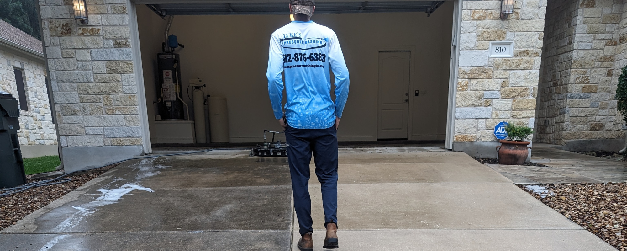 Luke’s Pressure Washing technician restoring a concrete driveway with high‑pressure cleaning, showing a clear before‑and‑after line