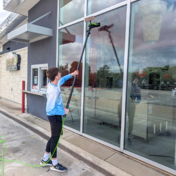 Technician from Luke’s Pressure Washing using a water-fed pole to clean tall commercial windows outside a drive-thru restaurant.